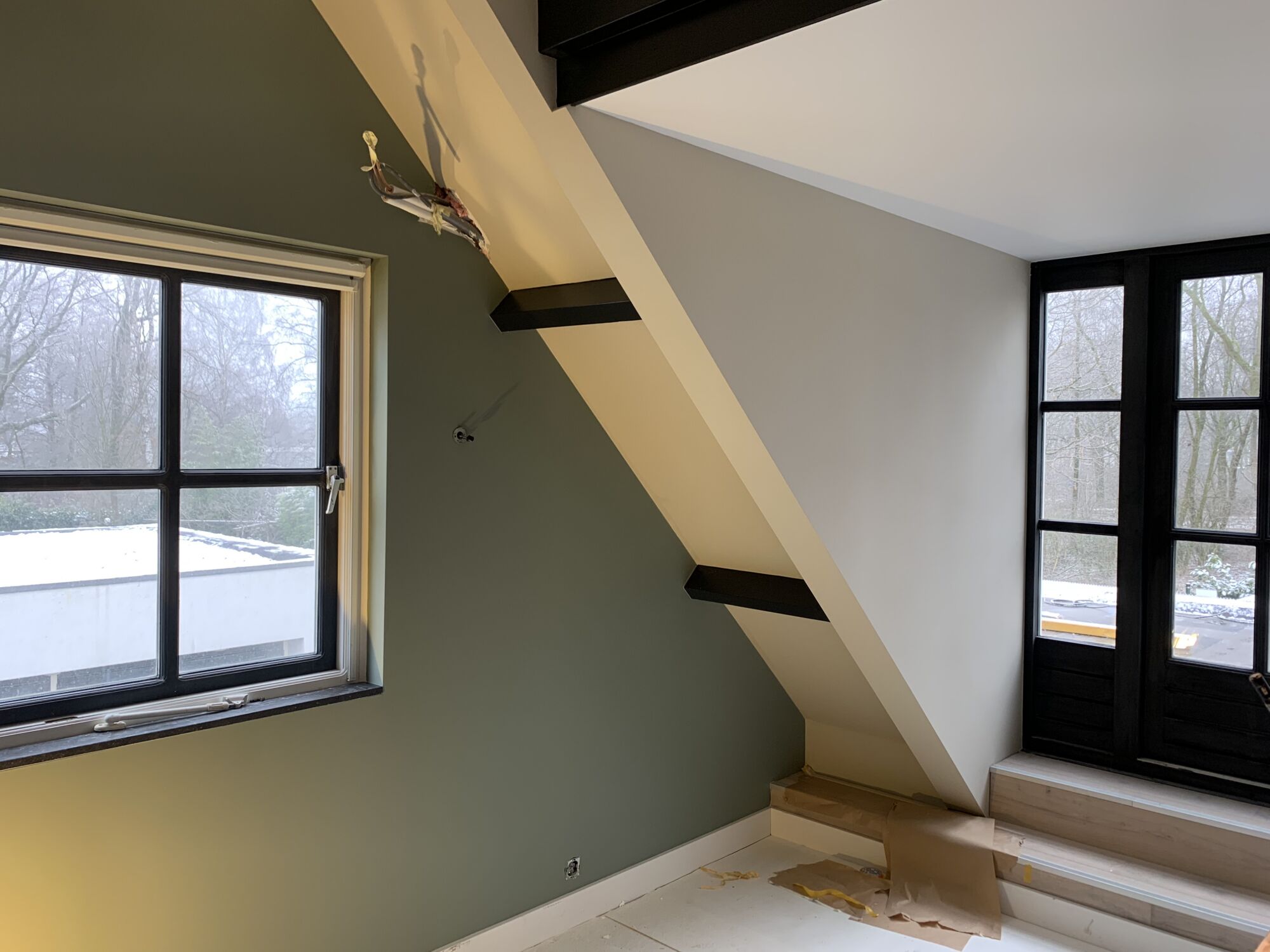 Zolderkamer met een groene wand, witte schuine wanden en zwarte kozijnen na het binnenschilderwerk